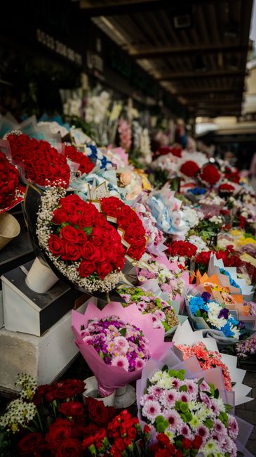 A vibrant display of fresh floral arrangements at a flower market, featuring a variety of bouquets with red roses, pink chrysanthemums, white lilies, and mixed pastel flowers wrapped in colorful paper